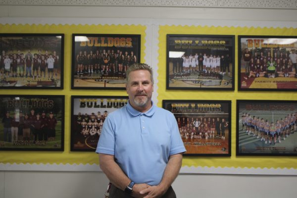 A posed photo of Randy Bell in the athletic director room, in front of team photos.