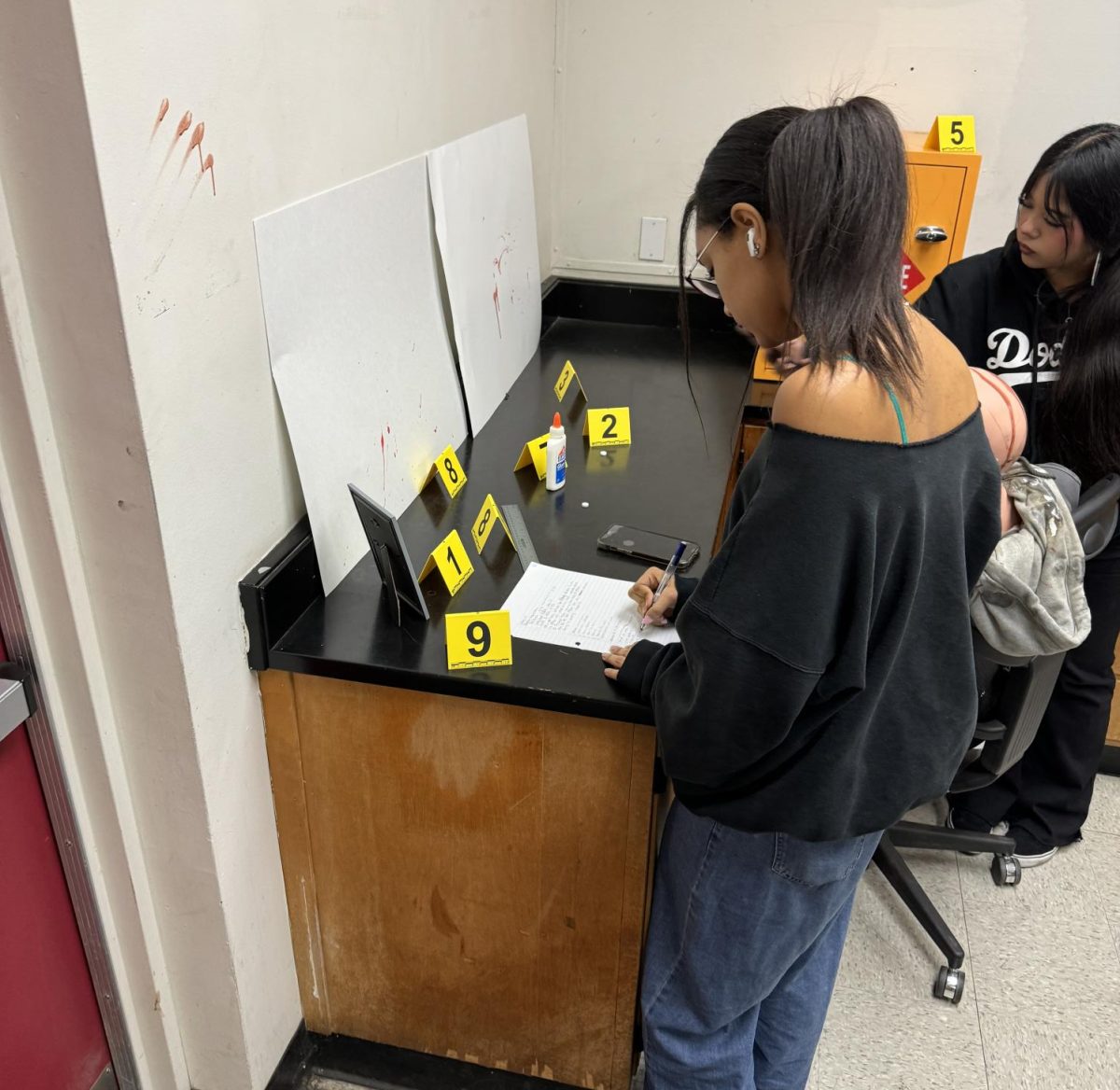 Students during a class activity where they have to describe what happened during a crime scene and take notes about the evidence found, specifically what time it was found and what it looks like. 