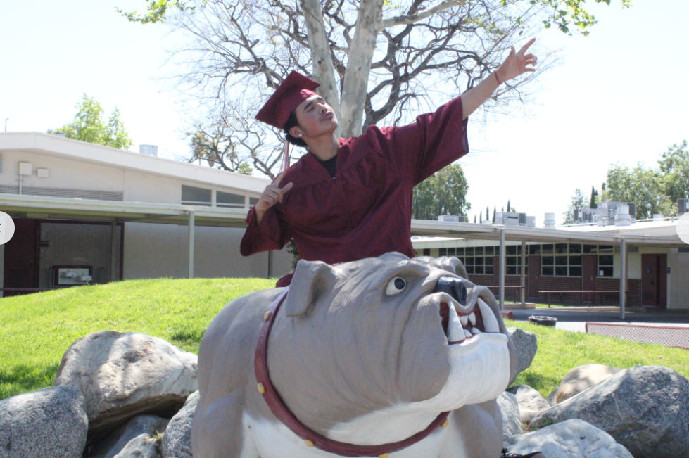 Senior Christian Orozco poses in a gradation cap and gown on West Covina High School bulldog mascot. 