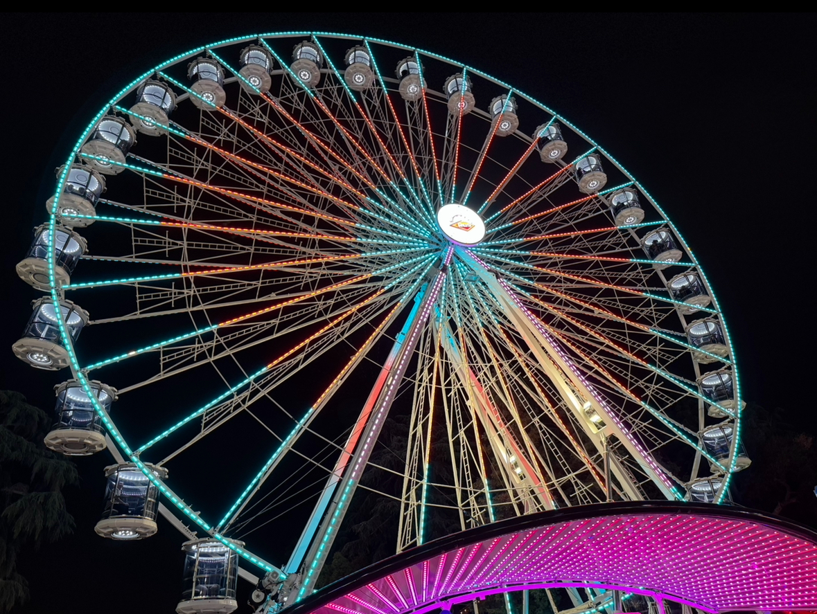 One of the three popular ferris wheels found near the back of the fair lit up by the many colorful lights. People on this attraction get a nice overview of the fair or a break from walking around.