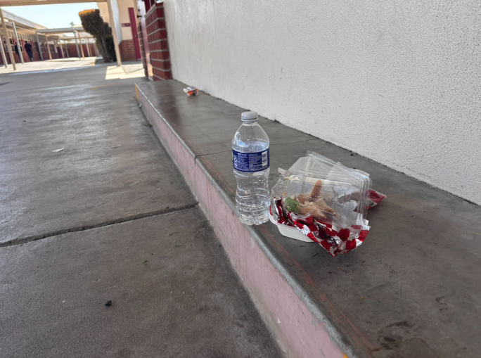 In the L hallway, a student leaves their trash behind after lunch even though a few feet away is a trash can.