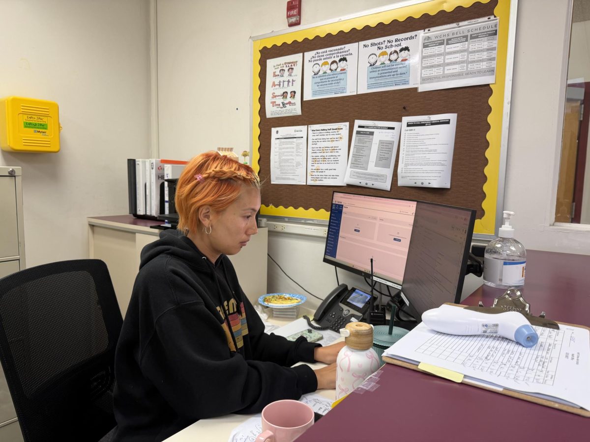 In the health office during lunch, Jade Rowe works at her desk. “So, if you have the stomach ache, headache, just to make sure that you're alright, and then when we have school guidelines to follow, like, if you're sick, if you throw up… wellness is taken care of, and then I can contact parents…”